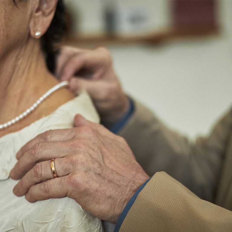 man-adjusting-necklace-on-elderly-woman-in-white-b-2025-07-04-16-20-04-utc