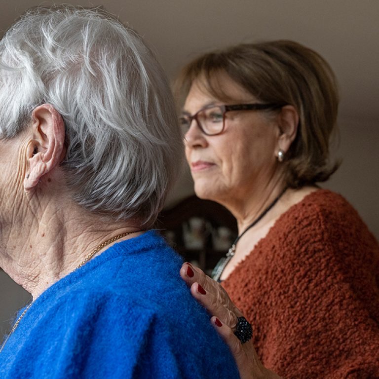 two-elderly-friends-standing-looking-out-of-the-wi-2025-04-03-22-21-33-utc